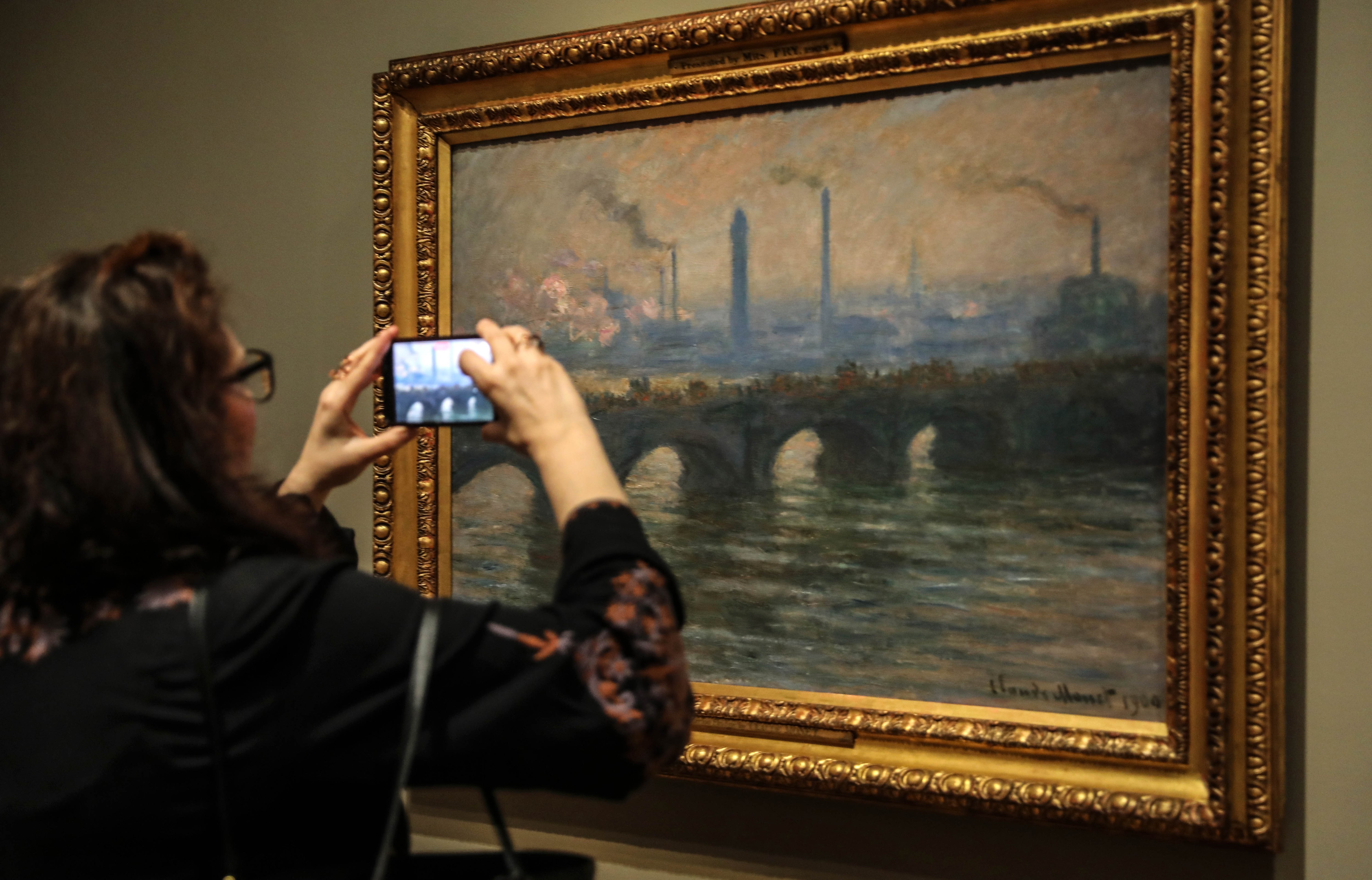 A visitor photographs a Monet painting of a London bridge.