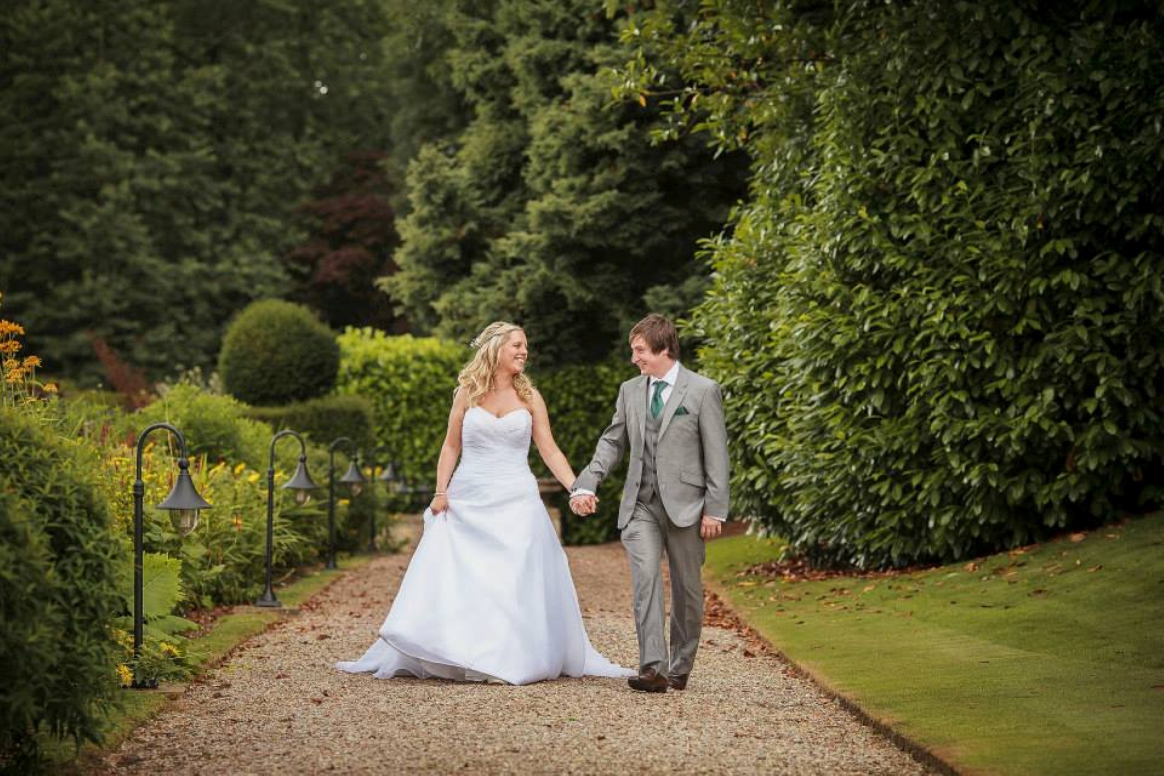 Bride and groom walking hand-in-hand down a garden path.