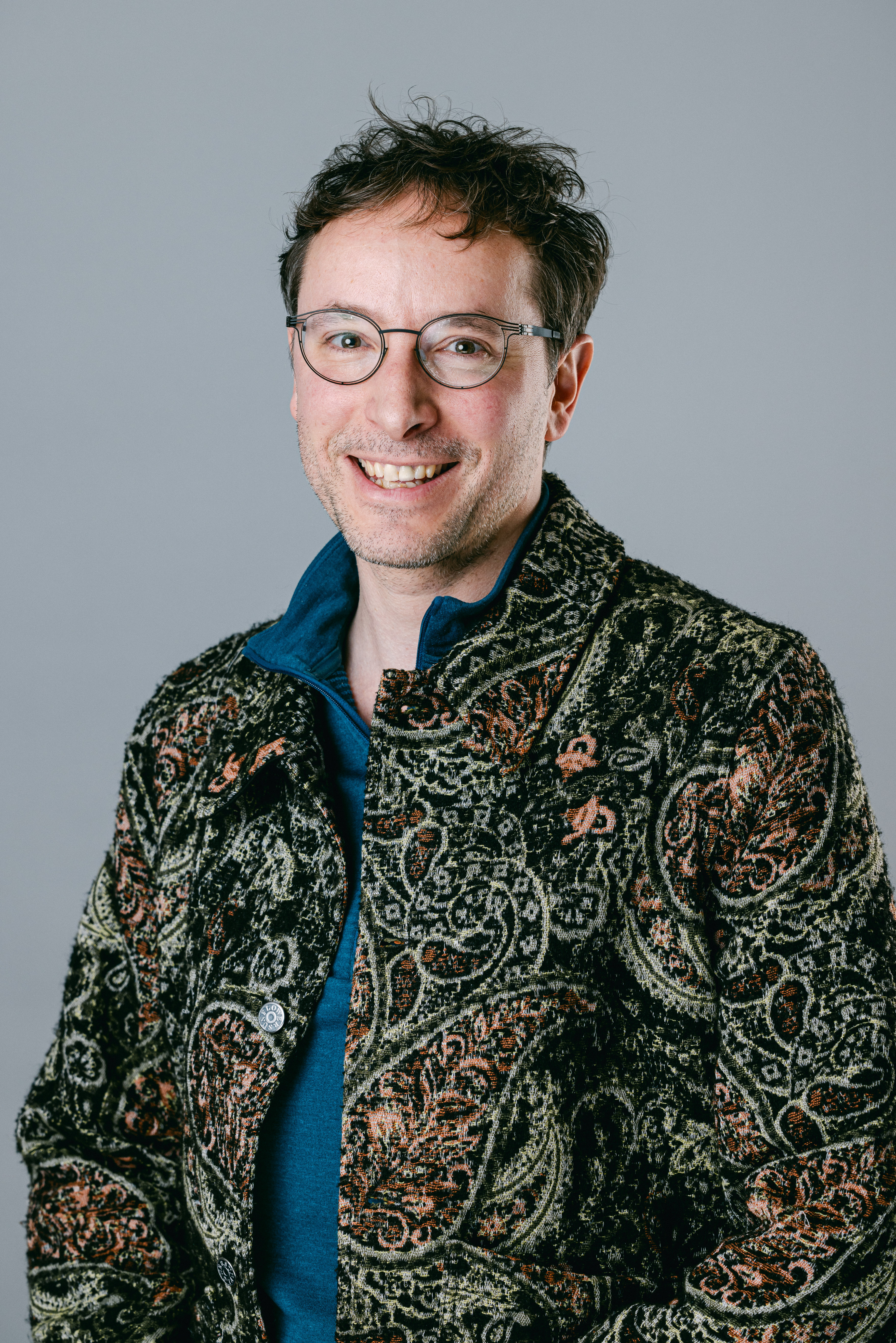 Portrait of a smiling man wearing glasses and a patterned jacket.