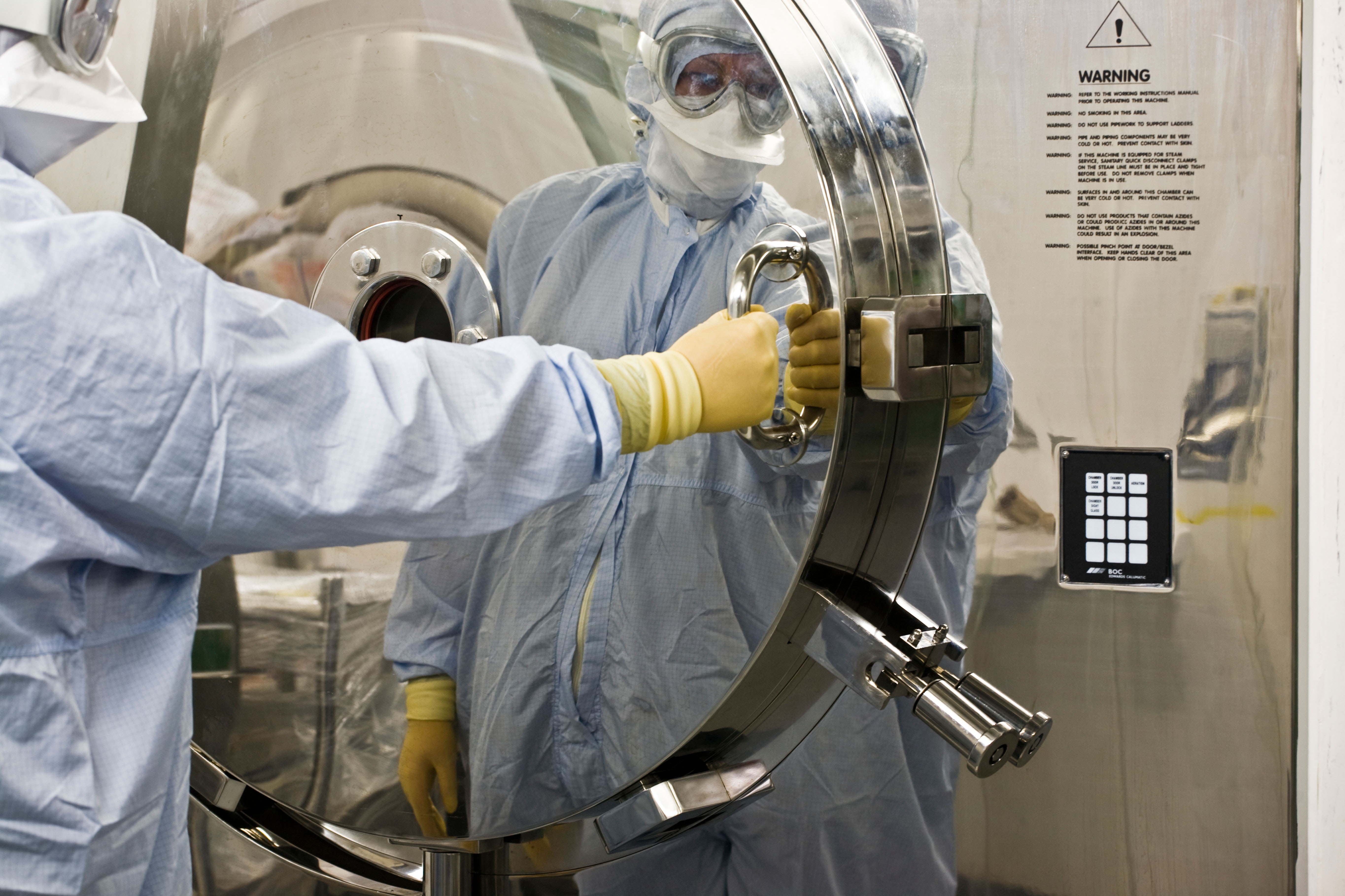 Workers in protective suits operating pharmaceutical machinery.
