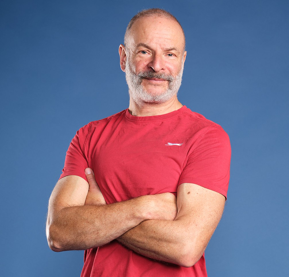 Фил Хилтон, arms crossed, wearing a red shirt and dark pants.