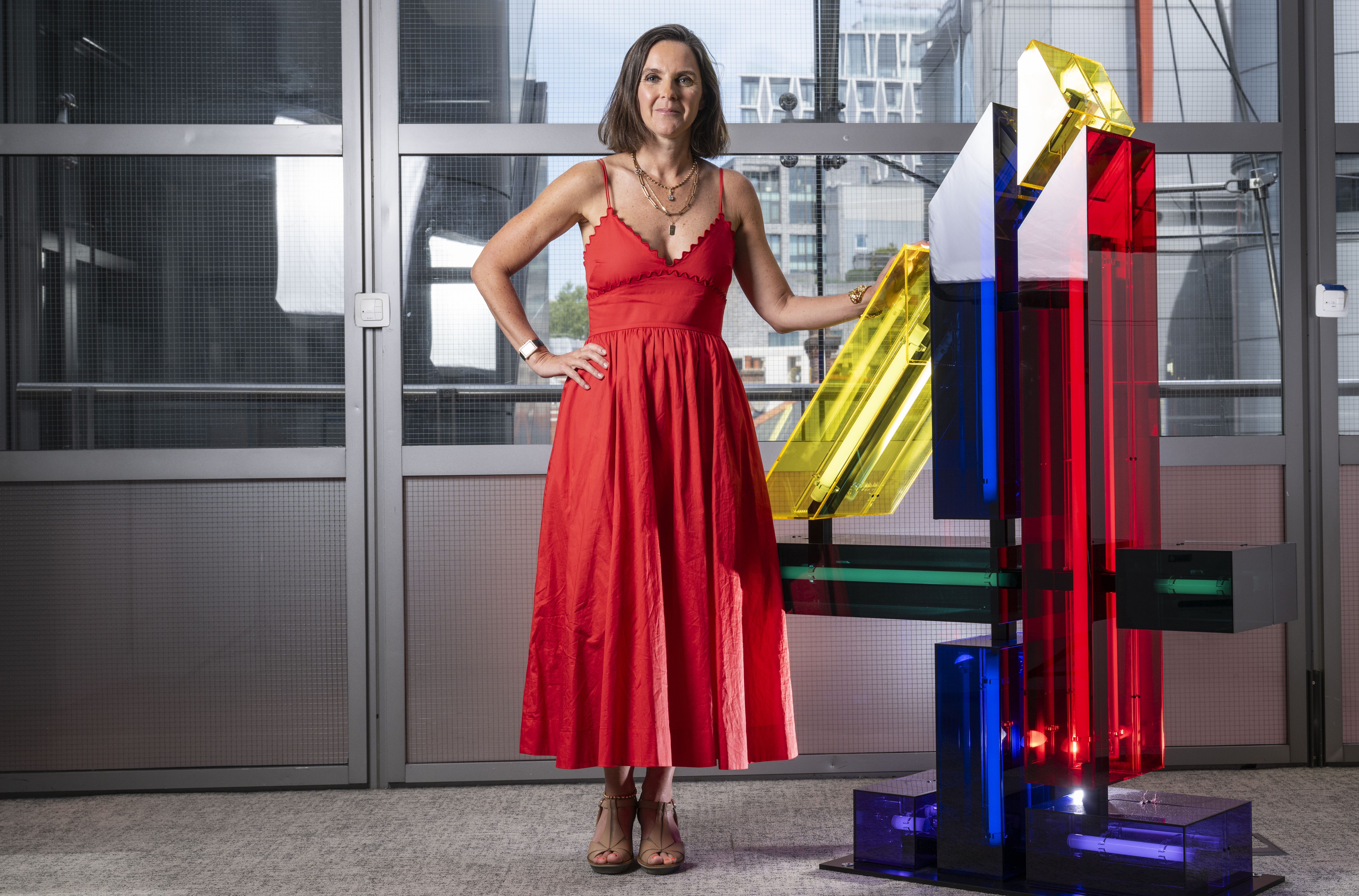 Алекс Махон, генеральный директор Channel 4, стоя рядом с цветной скульптурой.