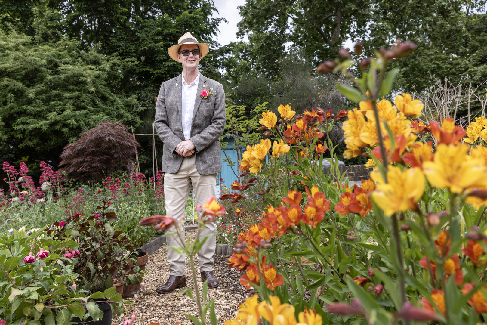 Человек в костюме стоит в саду на выставке RHS Chelsea Flower Show.