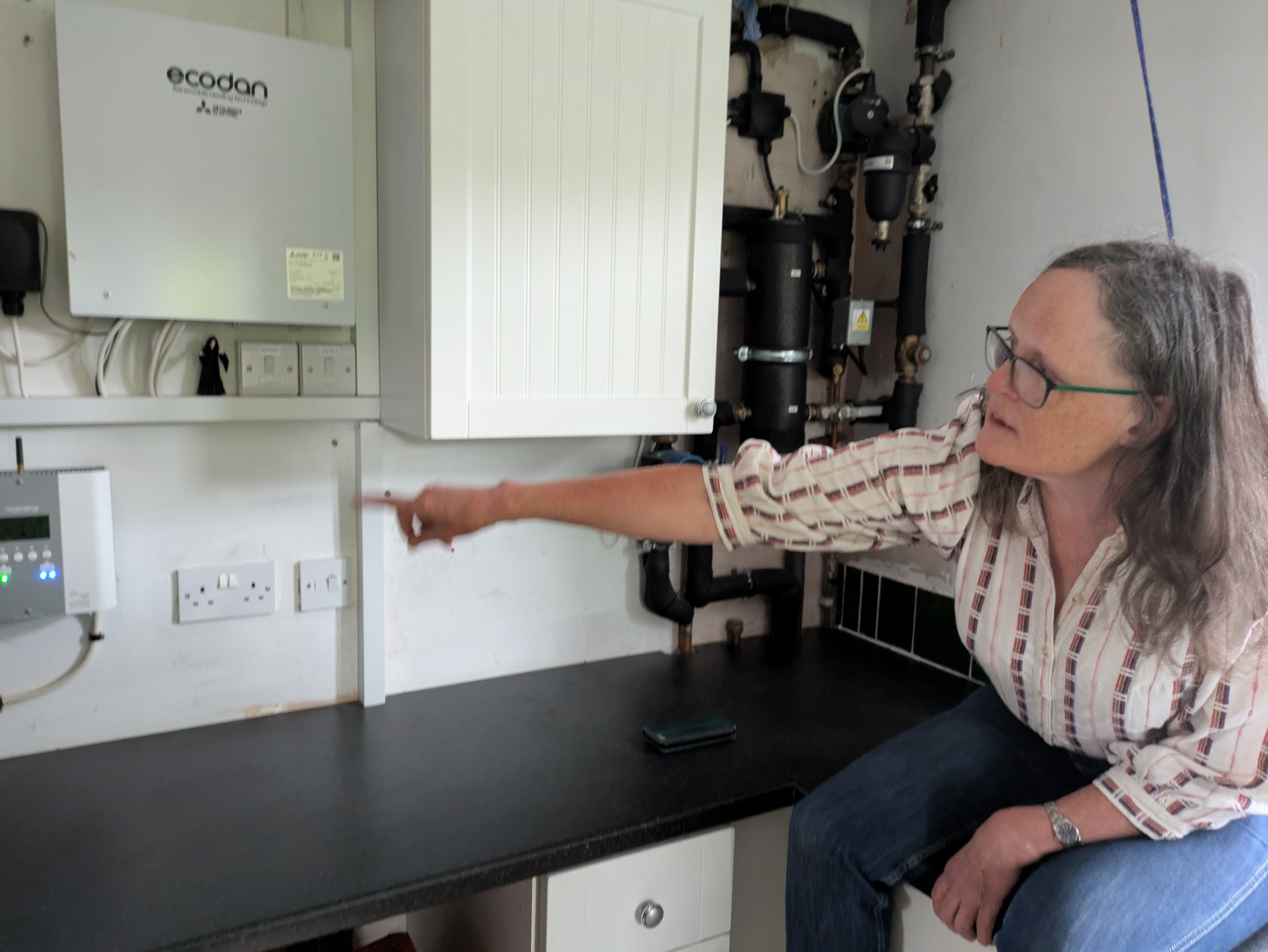 Женщина указывает на систему теплового насоса в utility room.