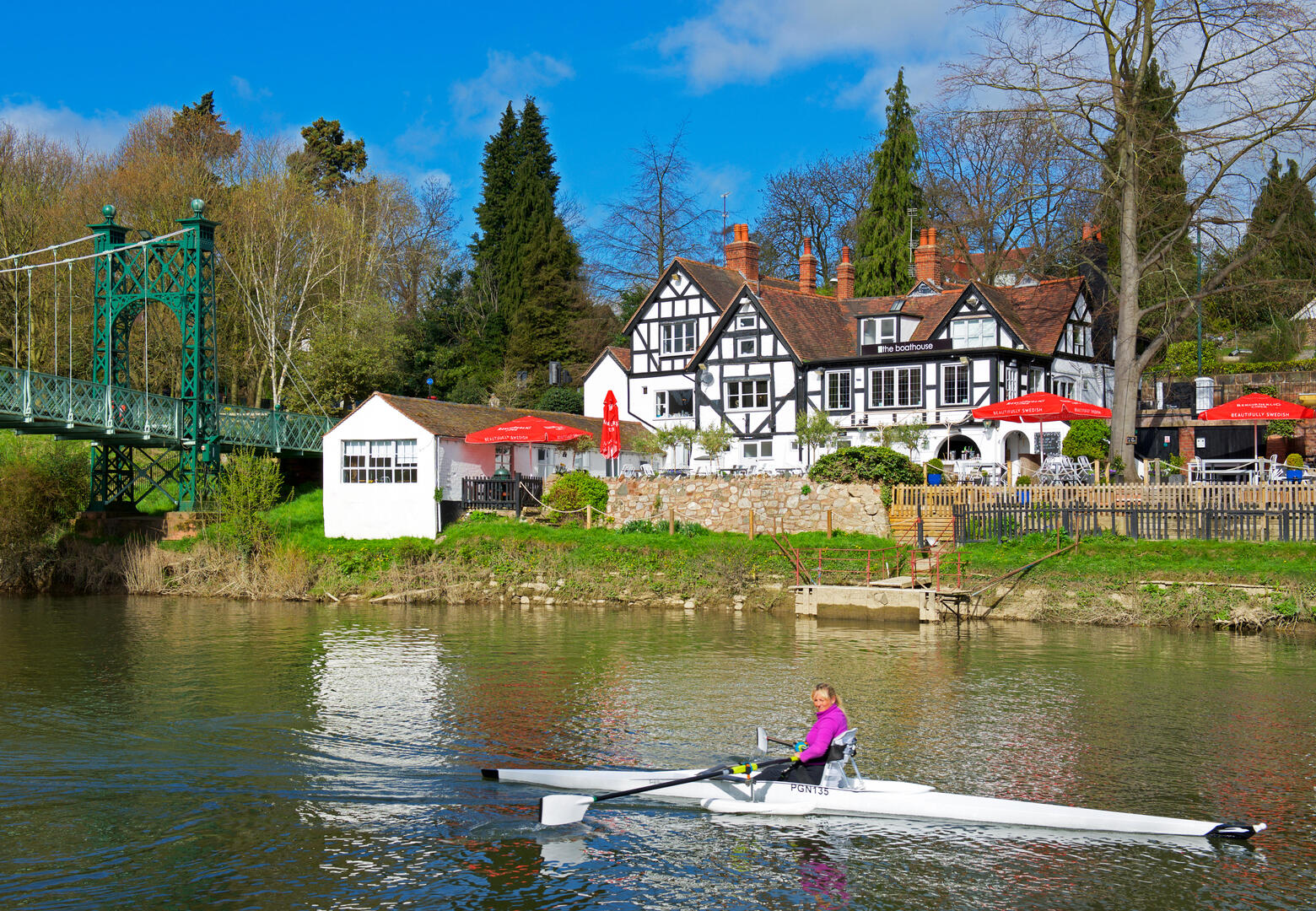 Гребец в лодке проходит мимо паба The Boathouse на реке Северн в Шрусбери, Англия.