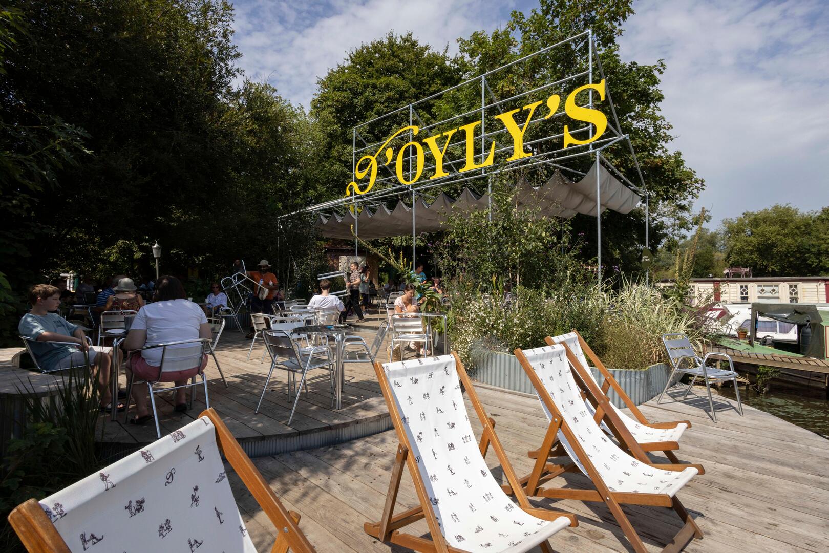 Люди сидят за столами на улице D'Oyly's, ресторана на палубе с видом на канал.