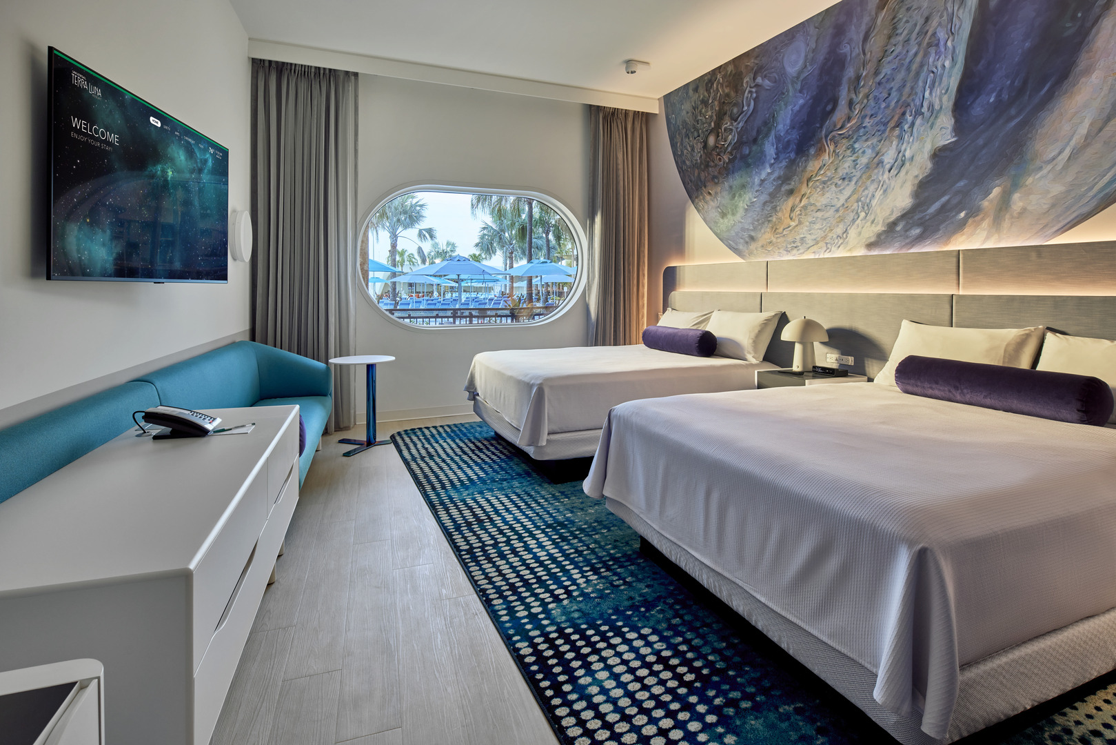 Номер для гостей Universal Terra Luna Resort с двумя кроватями, бирюзовым диваном и большим окном с видом на бассейн.