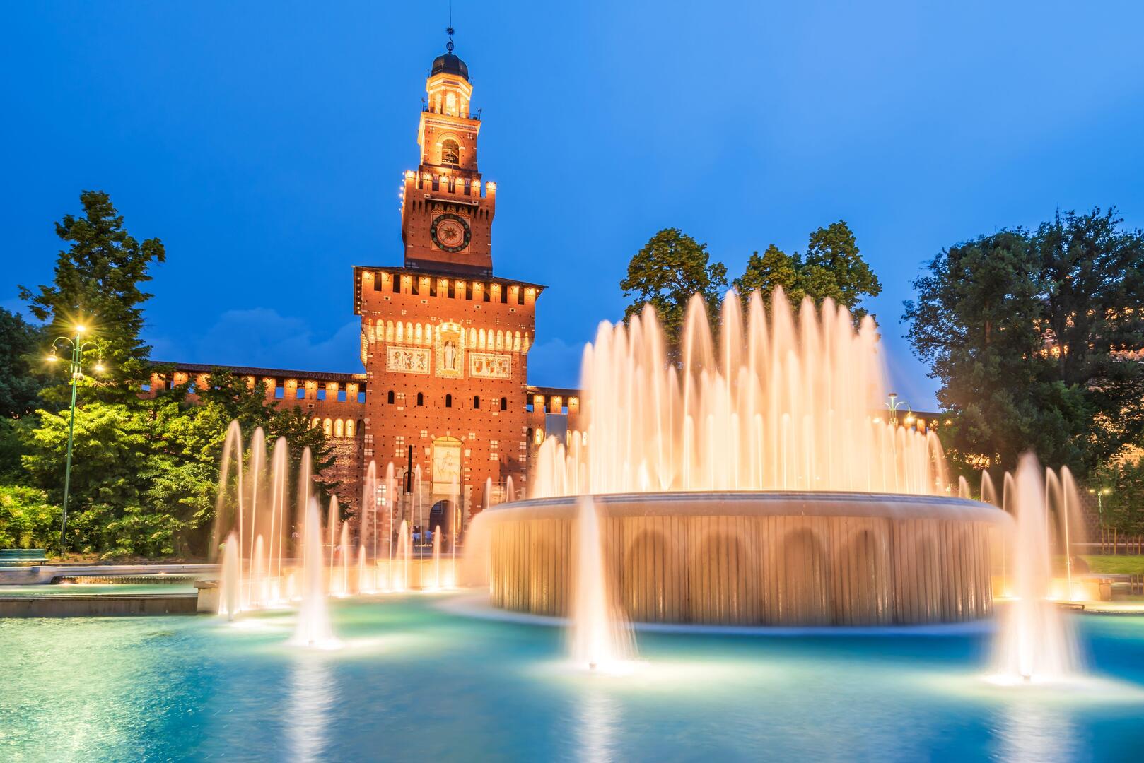 Sforza Castle in Milan at night, with a large fountain in the foreground.