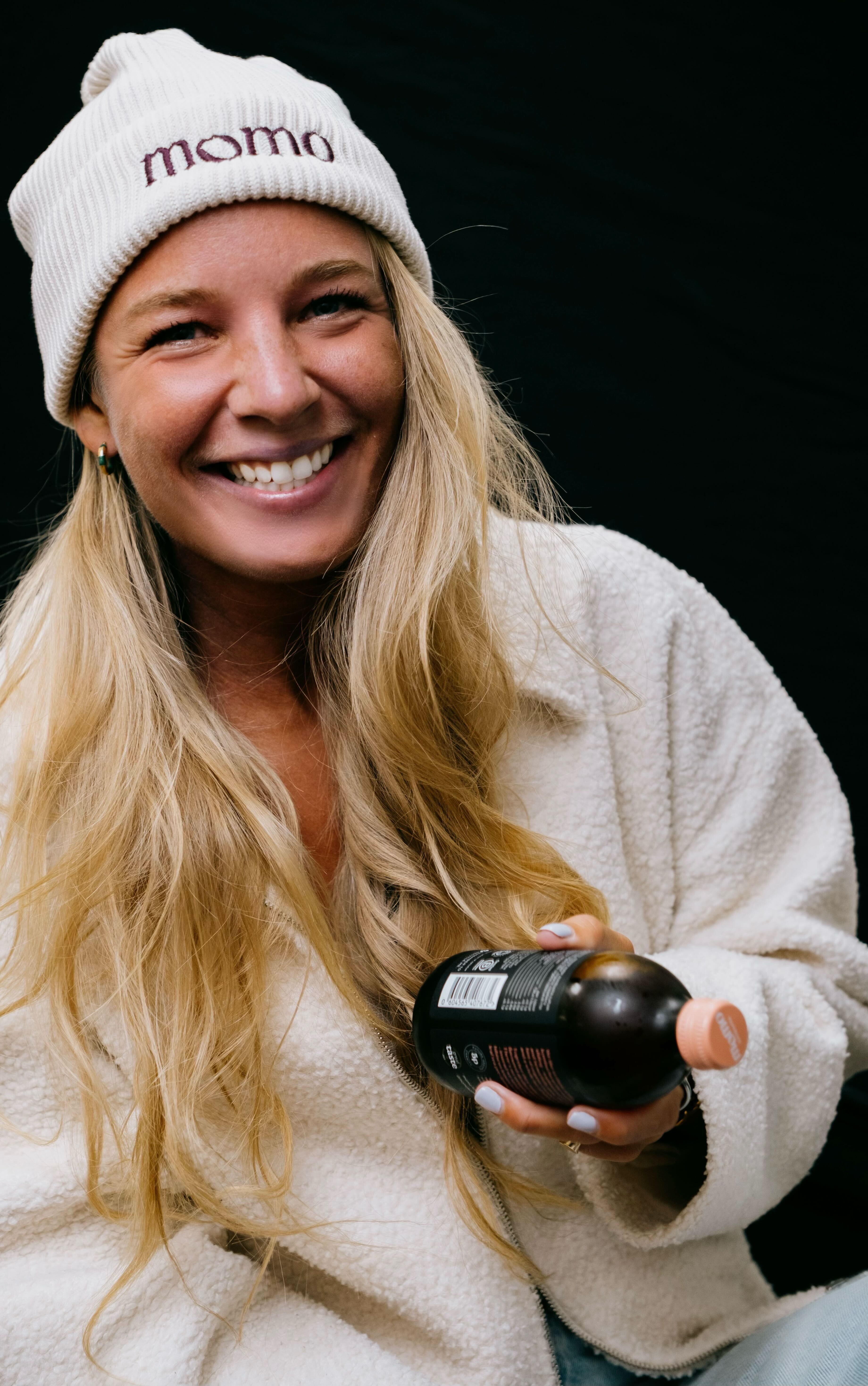 Woman wearing a Momo beanie holding a bottle.