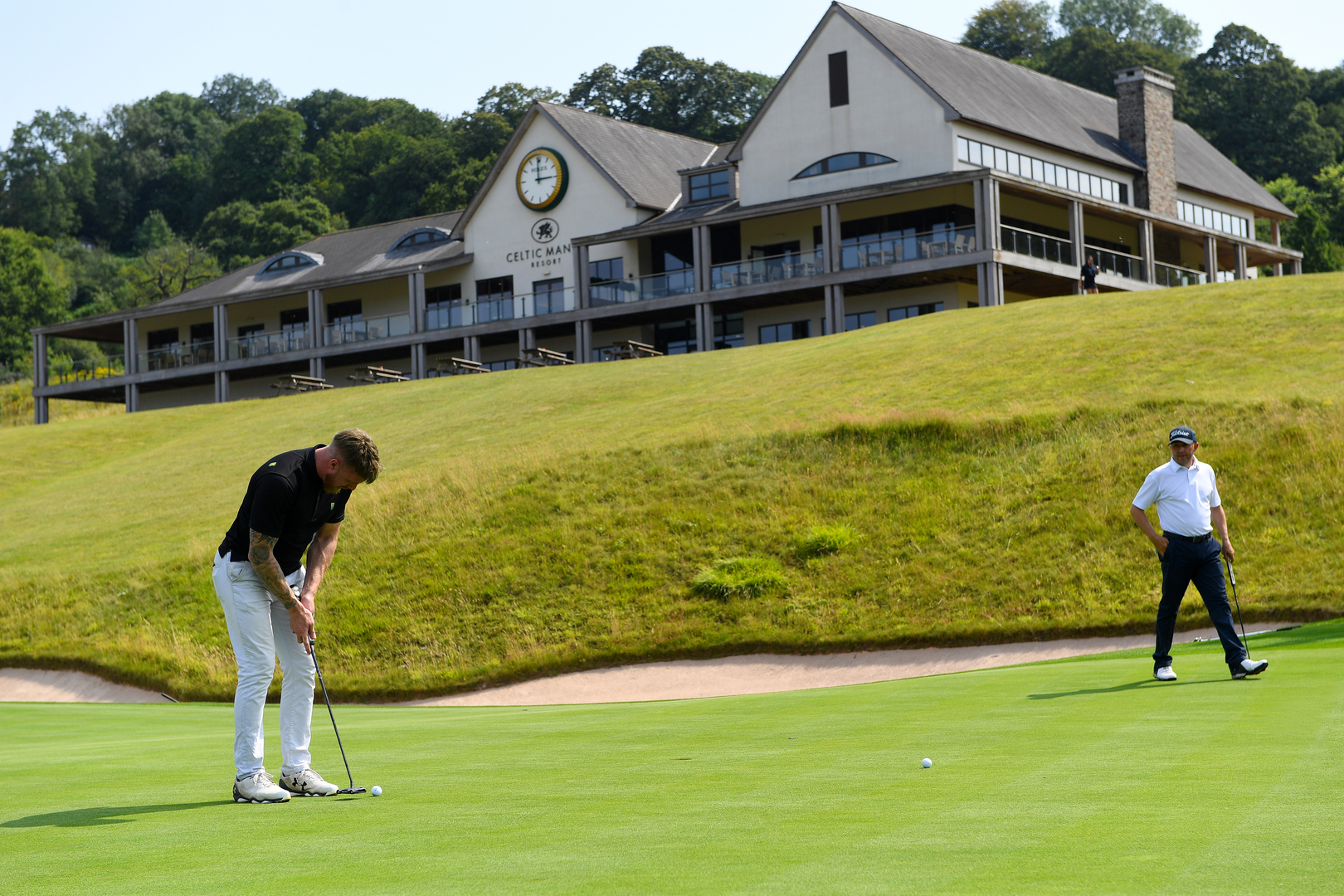 Два гольфера, выполняющих удар по лужайке в курорте Celtic Manor.