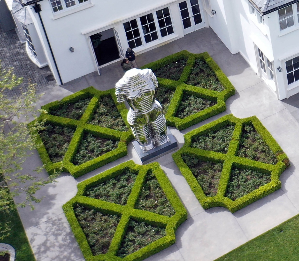 Aerial view of a chrome torso statue in a formal garden.